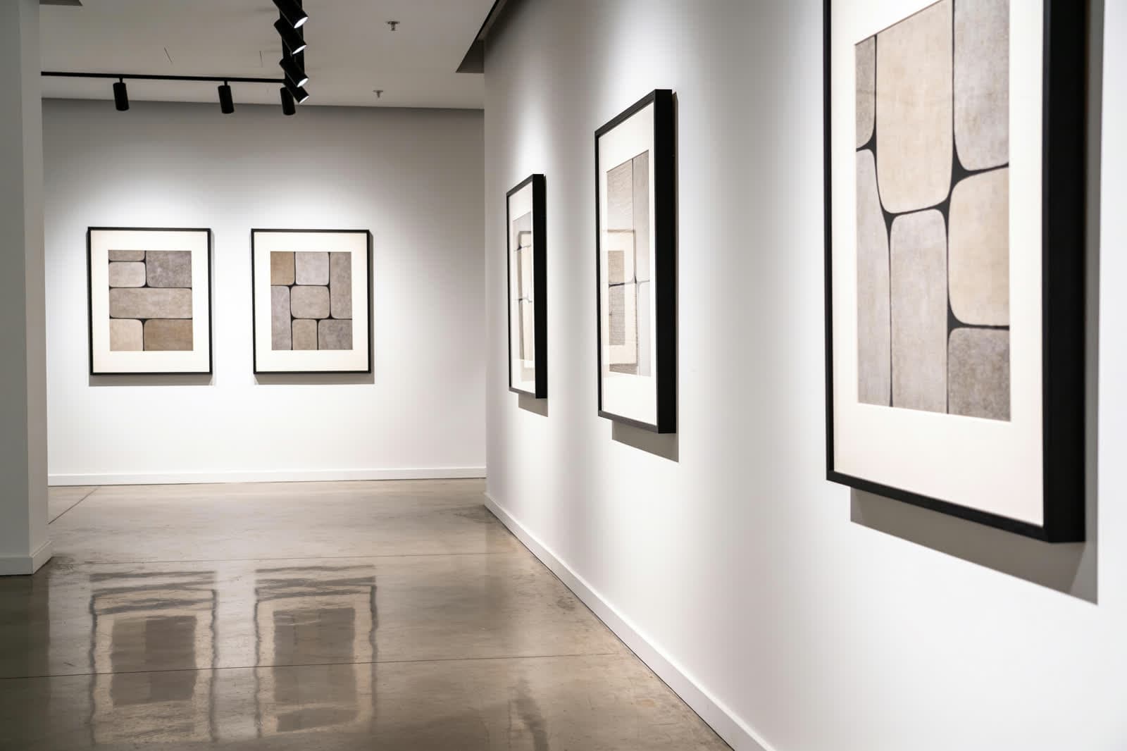 Galería de arte contemporáneo con obras abstractas enmarcadas, iluminación de riel y piso de concreto pulido