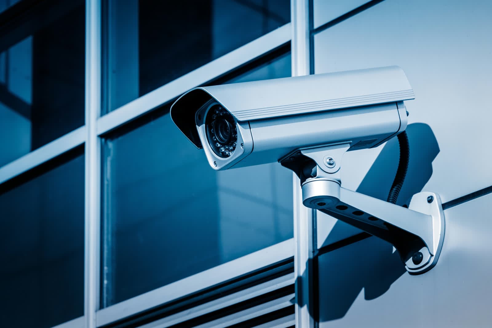 Cámara de videovigilancia moderna montada en la fachada de vidrio azul de un edificio comercial